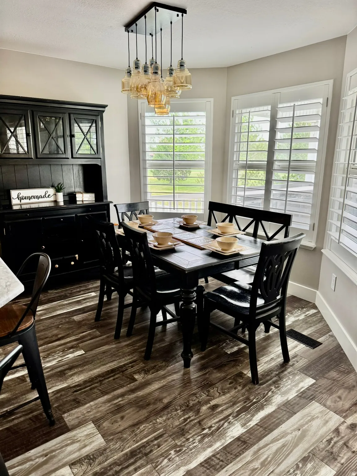 Dining area with wood-finish flooring, a contemporary multi-bulb chandelier, and multiple windows featuring plantation shutters