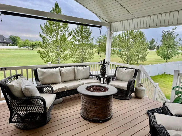 Expansive covered deck featuring wood-finish flooring, a white railing, and a built-in stone-look fire pit