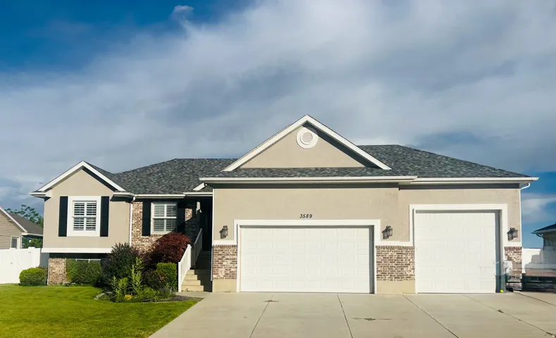 Multi-level stucco exterior featuring brick accents, dark shutters, and a two-car garage