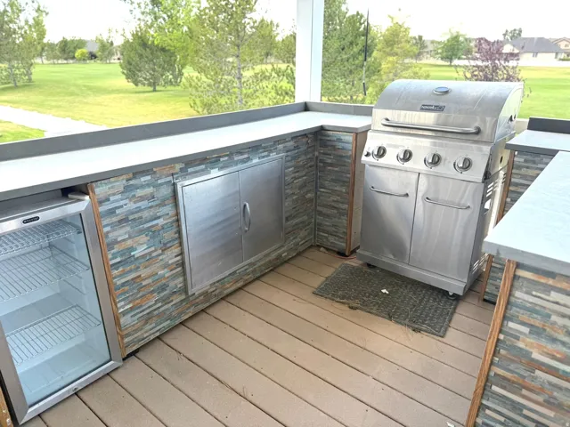 Outdoor kitchen featuring a built-in stainless steel grill, integrated under-counter refrigerator, ample counter space, and stacked stone veneer accents