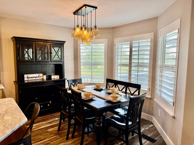 Dining area featuring wood-finish flooring, a contemporary multi-light pendant fixture, and a bay window configuration with white louvered shutters