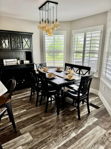 Dining area with wood-finish flooring, a contemporary multi-bulb chandelier, and multiple windows featuring plantation shutters