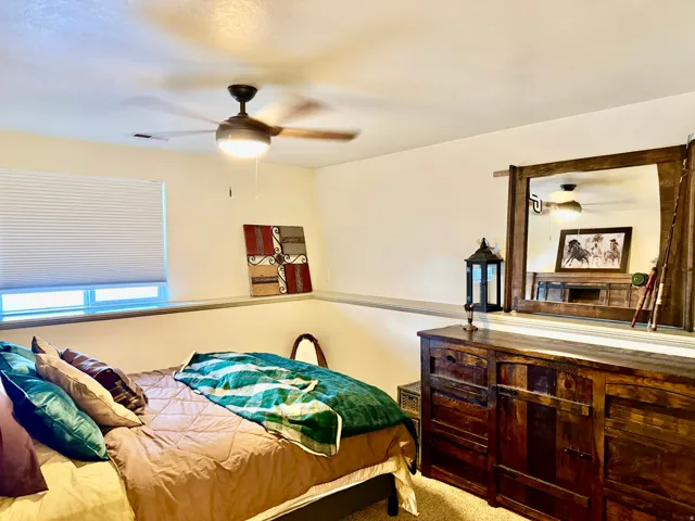 Bedroom featuring plush carpeting, a large window with privacy blinds, and a ceiling fan with integrated lighting