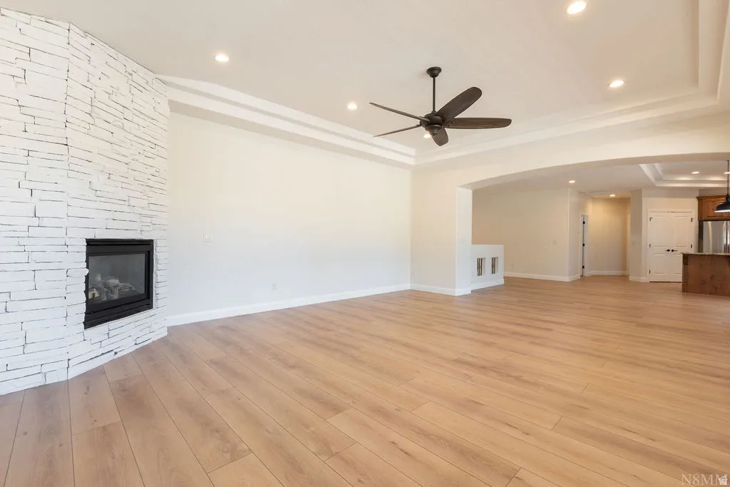 Spacious room featuring wood-finish flooring, a contemporary fireplace with stacked stone surround, recessed lighting, and a ceiling fan