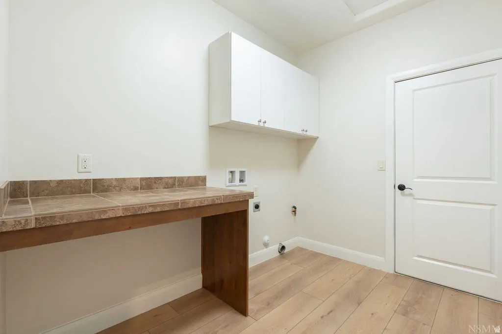 Laundry room featuring wood-finish flooring, white cabinetry, a tiled countertop with backsplash, and a paneled white door