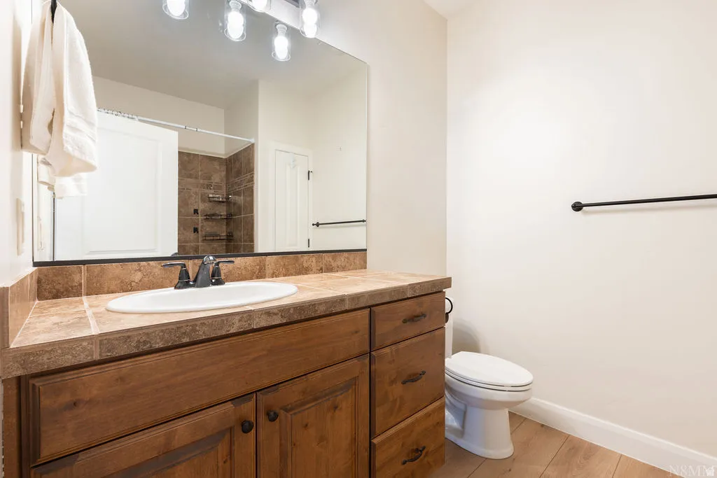 Bathroom featuring a wood-finish vanity with a tiled countertop, undermount sink, and black fixtures