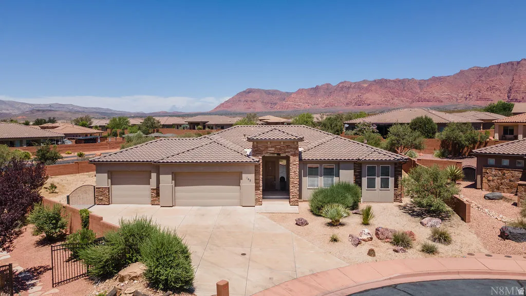 Contemporary stucco and stone-clad residence featuring a tile roof, three-car garage, and desert-adapted landscaping