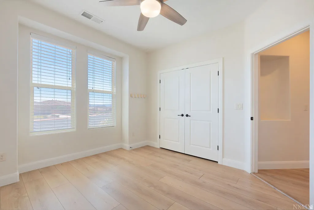 Bright interior space featuring light wood-finish flooring, white baseboards, and a ceiling fan with integrated lighting
