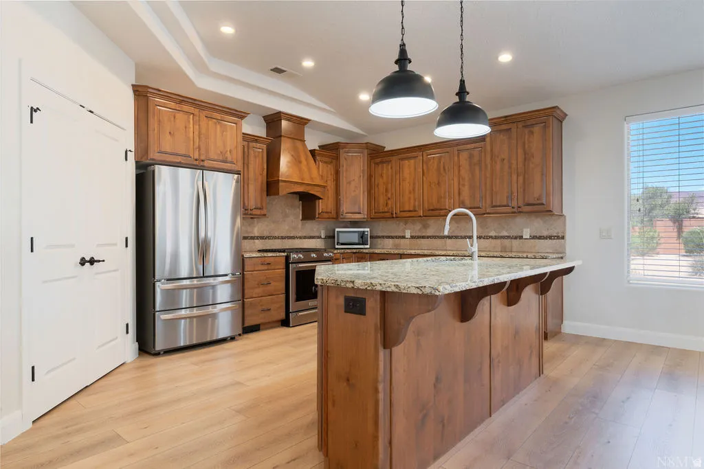 Kitchen showcasing wood cabinetry, granite countertops, stainless steel appliances, and wood-finish flooring