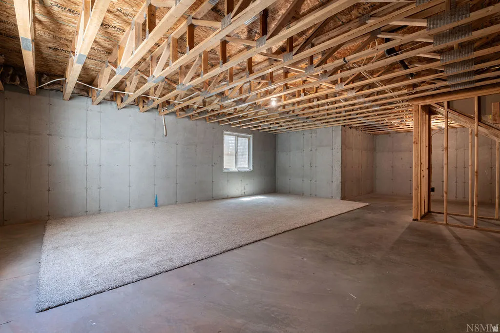 Unfinished basement featuring exposed wood ceiling joists, concrete walls, a single window, and a partial carpeted area