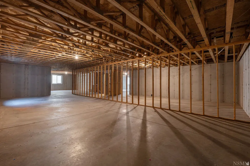 Unfinished basement featuring concrete flooring, exposed ceiling joists, wood framing for partitioning, and a visible window