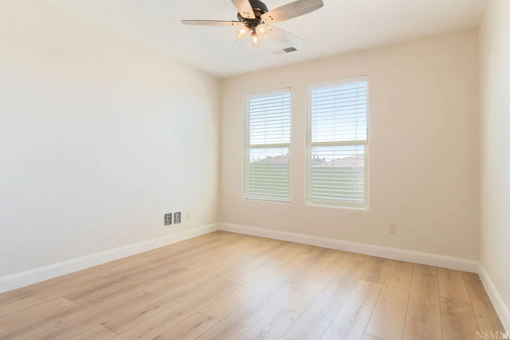 Bright interior space featuring wood-finish flooring, two windows with blinds, a ceiling fan with integrated lighting, and white baseboards