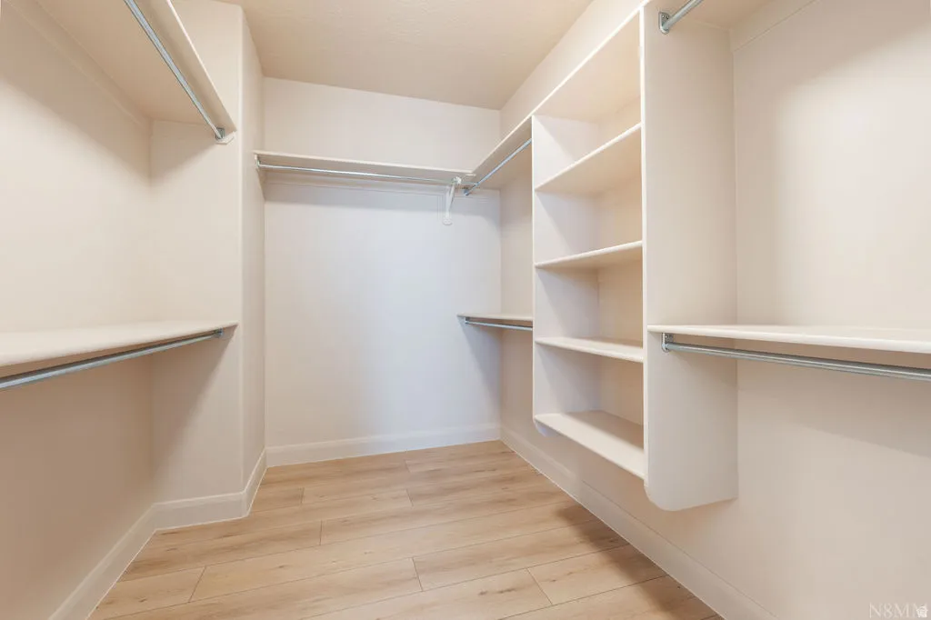 Walk-in closet featuring light wood-finish flooring, white walls, built-in shelving, and multiple hanging rods for organization