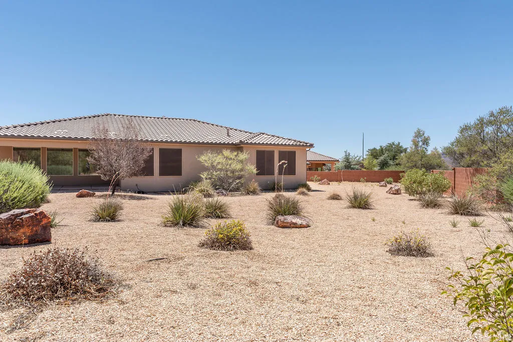 Spacious xeriscaped backyard featuring a gravel landscape, desert-adapted plantings, natural rock elements, and a perimeter wall