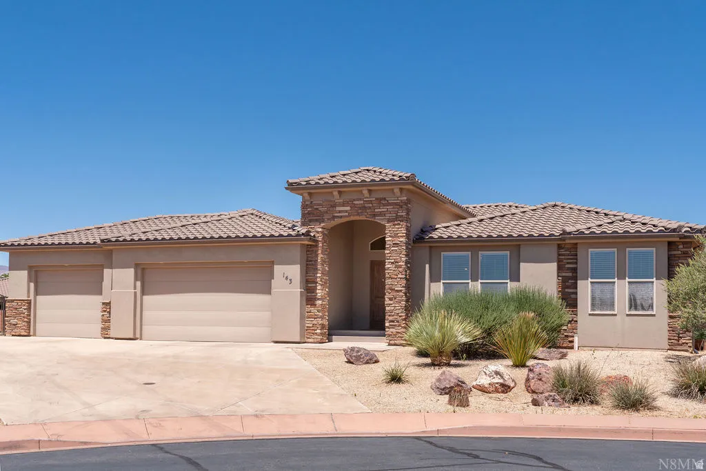 Stucco and stone exterior featuring an arched entry, tile roof, dual garage doors, and xeriscaped landscaping