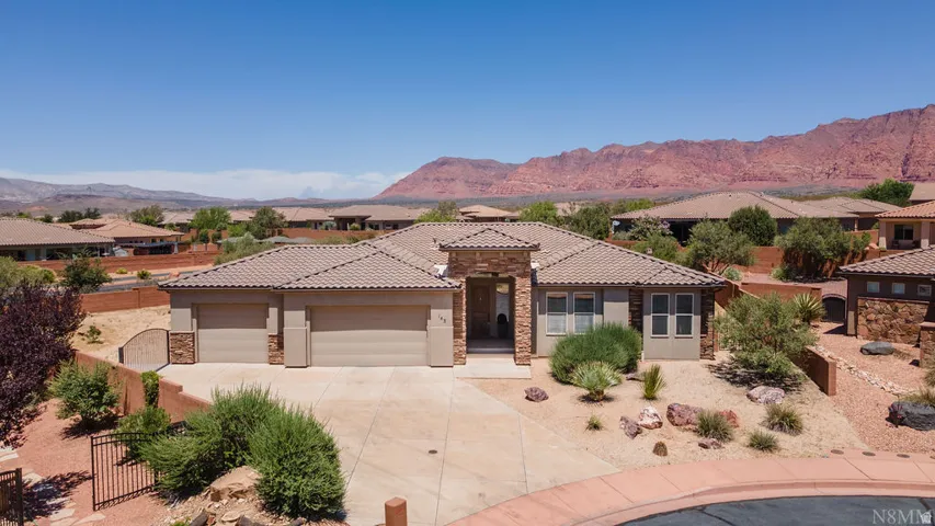 Contemporary stucco and stone-clad residence featuring a tile roof, three-car garage, and desert-adapted landscaping