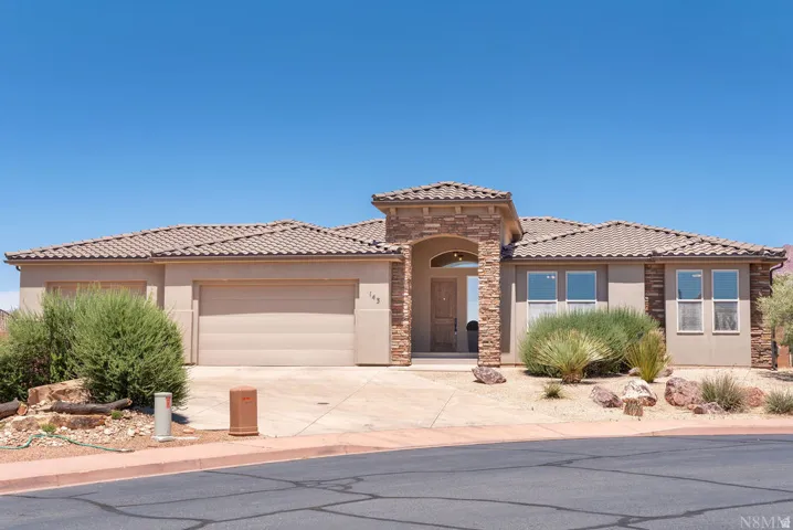 Stucco exterior home featuring a tile roof, an arched stone entry, an integrated two-car garage, and desert-style landscaping