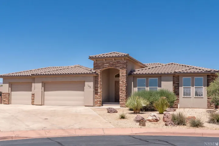 Stucco and stone exterior featuring an arched entry, tile roof, dual garage doors, and xeriscaped landscaping