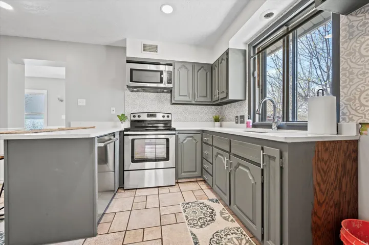 Kitchen featuring grey cabinetry, stainless steel appliances, white countertops, tile flooring, and a patterned tile backsplash