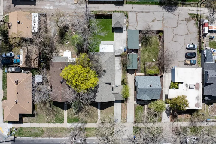 Aerial view showcasing multiple residential properties, featuring a mix of mature trees, paved driveways, and varied rooflines
