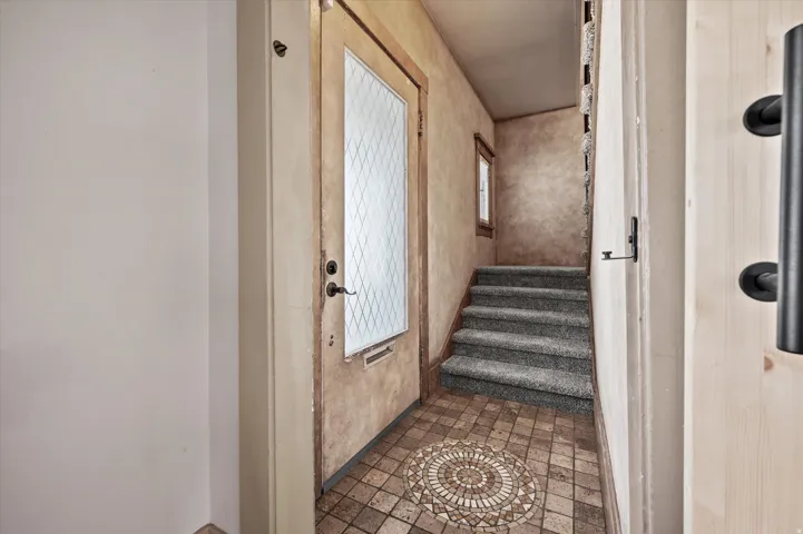 Entryway featuring a decorative mosaic tile floor, a front door with a diamond-patterned glass insert, and a carpeted staircase leading upwards