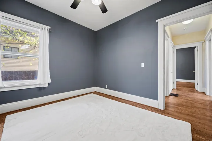 Room featuring wood-finish flooring, a ceiling fan, white baseboards, and a window with white trim