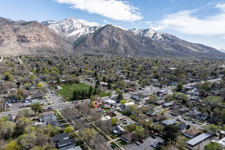 Aerial overview of a residential neighborhood with tree-lined streets, featuring a green space and a prominent mountain range with snow-capped peaks in the background