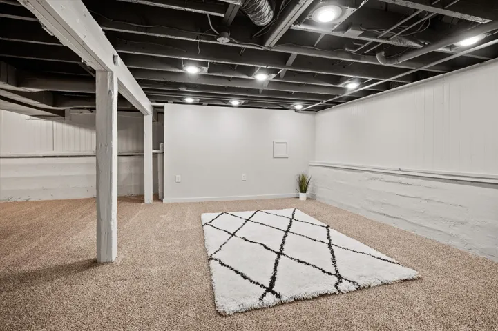 Expansive basement featuring exposed ceiling joists, recessed lighting, carpeted flooring, and painted paneled walls