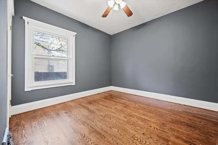 Room featuring wood-finish flooring, a white-trimmed window, a ceiling fan with light fixture, and dark gray wall finishes