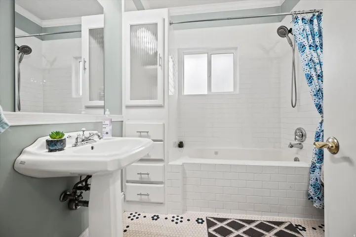 Bathroom featuring a pedestal sink, white subway tile shower surround, built-in cabinetry with reeded glass fronts, and black and white hexagon tile flooring