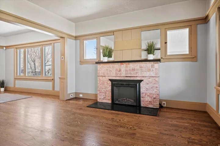 Living area featuring wood-finish flooring, a tiled fireplace with a black hearth, extensive wood trim, multiple windows, and a cased opening