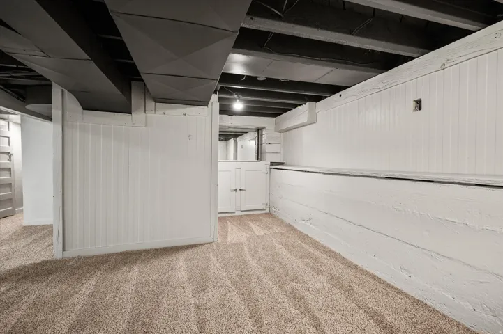Finished lower level featuring neutral carpet, painted paneling, exposed ceiling joists, and ductwork