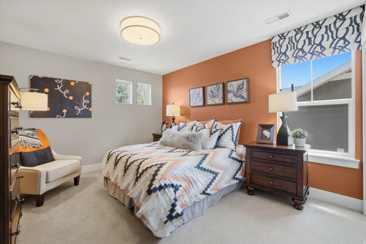 Carpeted bedroom featuring an accent wall, a window with a patterned roman shade, and two high casement windows