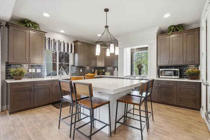Spacious kitchen featuring an expansive central island with seating, recessed lighting, wood-finish flooring, and dark cabinetry