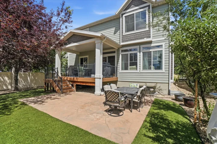 Expansive backyard featuring a covered deck, stamped concrete patio, artificial turf lawn, and mature trees