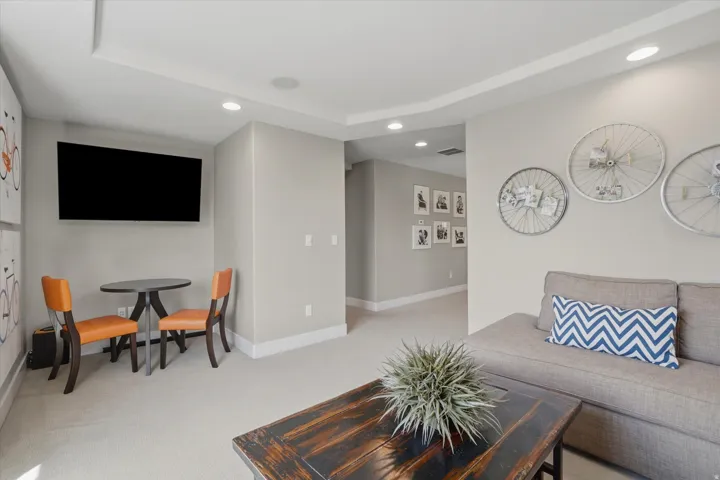 Recessed lighting illuminates this space featuring a mounted display, a light-colored carpet, and a hallway entrance