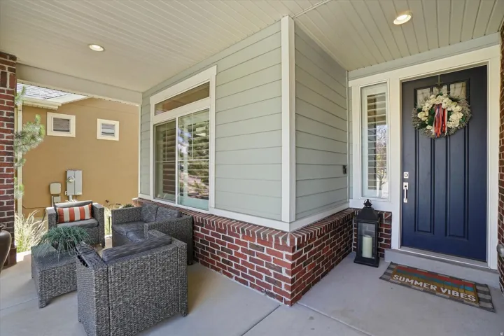 Covered front porch featuring a dark paneled entry door, light siding, and a brick facade