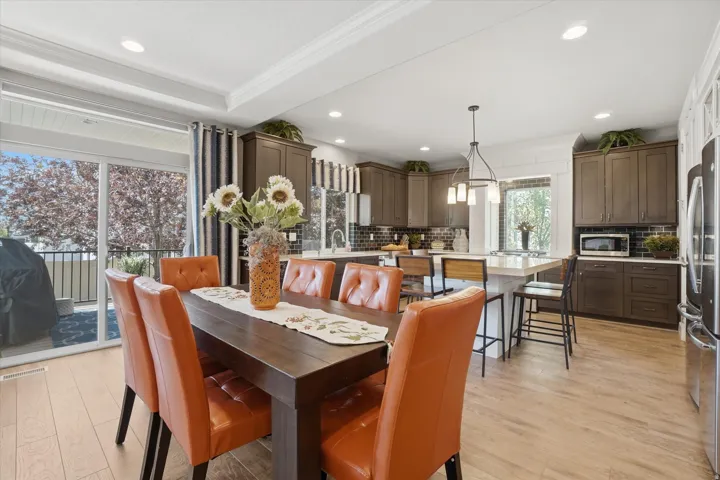 Open-concept kitchen and dining area featuring light wood-finish flooring, dark wood cabinetry, a central island with countertop seating, stainless steel appliances, and a glass sliding door leading to an outdoor balcony