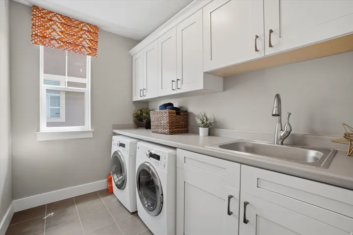 Laundry room featuring a window, built-in cabinetry, dual washer and dryer appliances, an integrated sink, and countertops