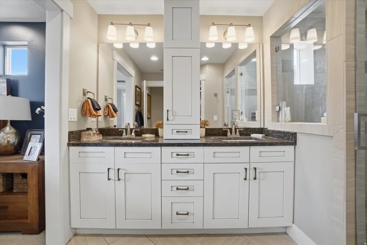 Double vanity featuring white shaker cabinetry, dark countertops, dual undermount sinks, and brushed nickel hardware