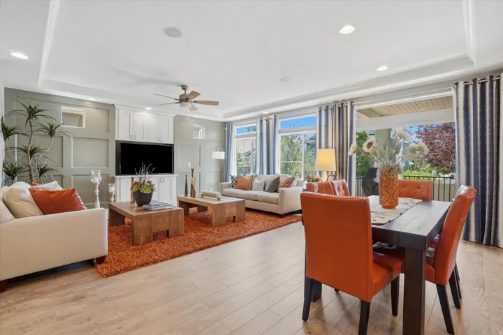 Open-concept living and dining area featuring wood-finish flooring, a tray ceiling with recessed lighting, and a built-in entertainment center with white cabinetry