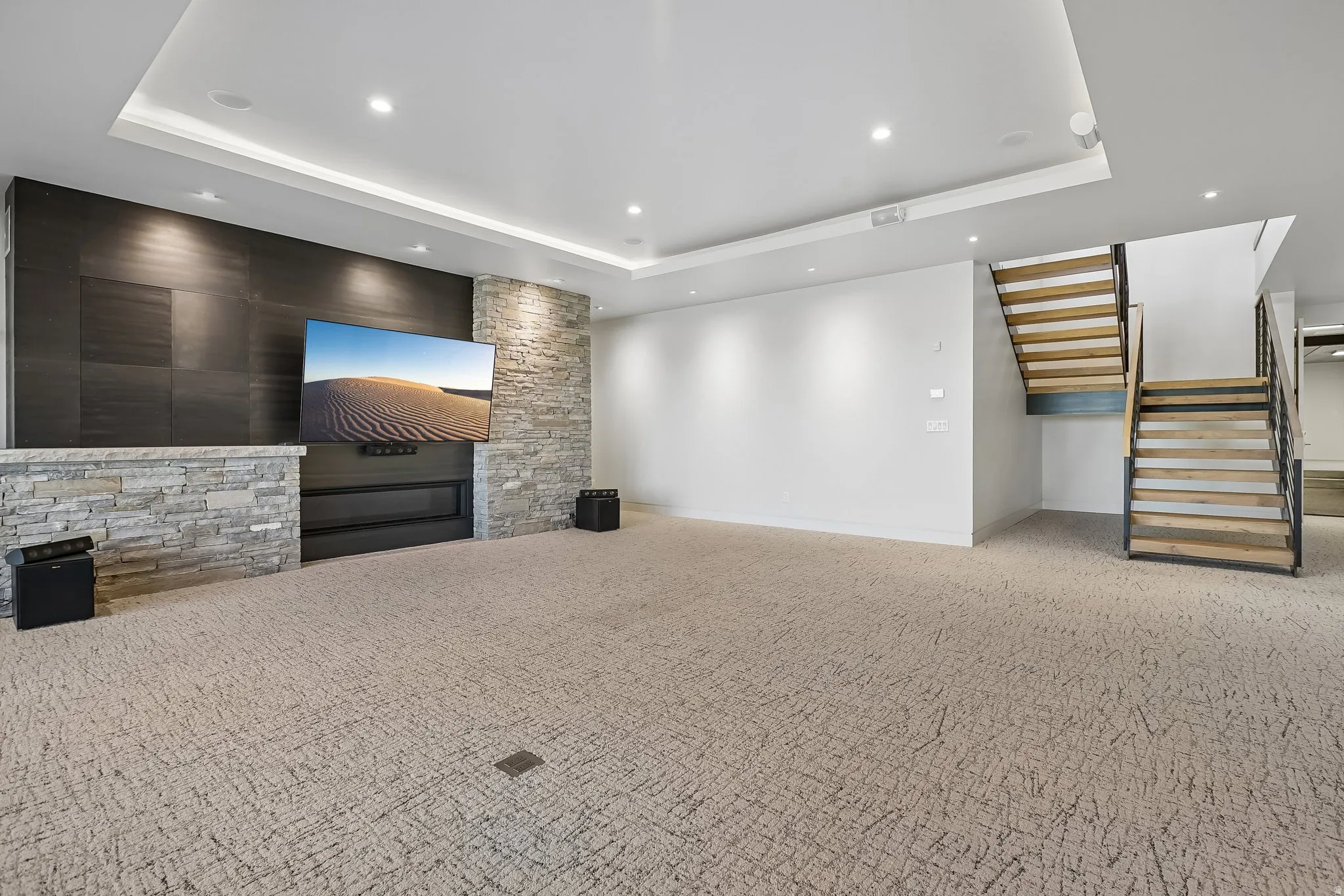 Spacious entertainment area featuring a contemporary fireplace with stone surround, accent wall, recessed lighting, and a floating staircase with wood treads and metal railings