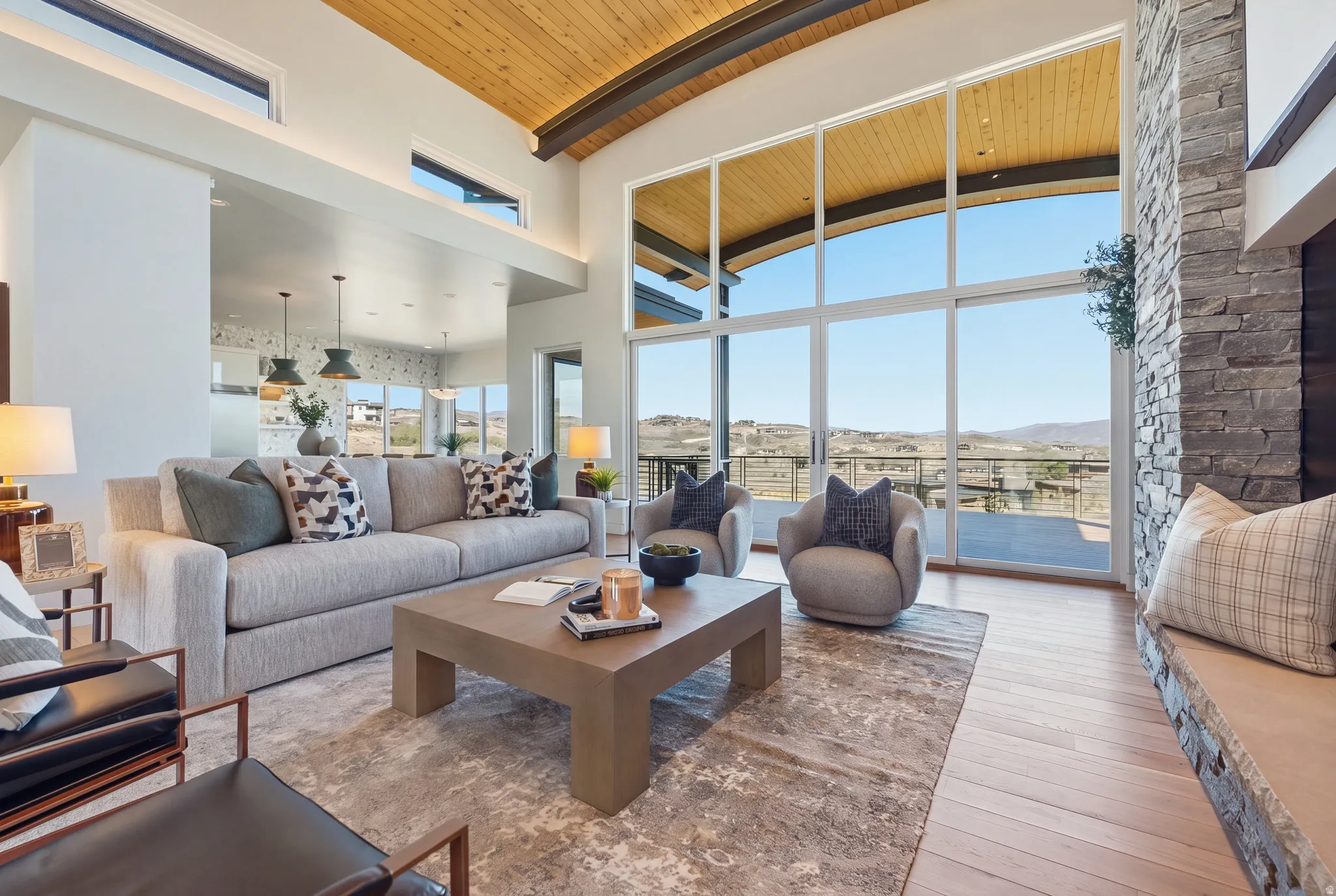 Vaulted wood-paneled ceiling, floor-to-ceiling windows, stone-clad fireplace with hearth, and wood-finish flooring