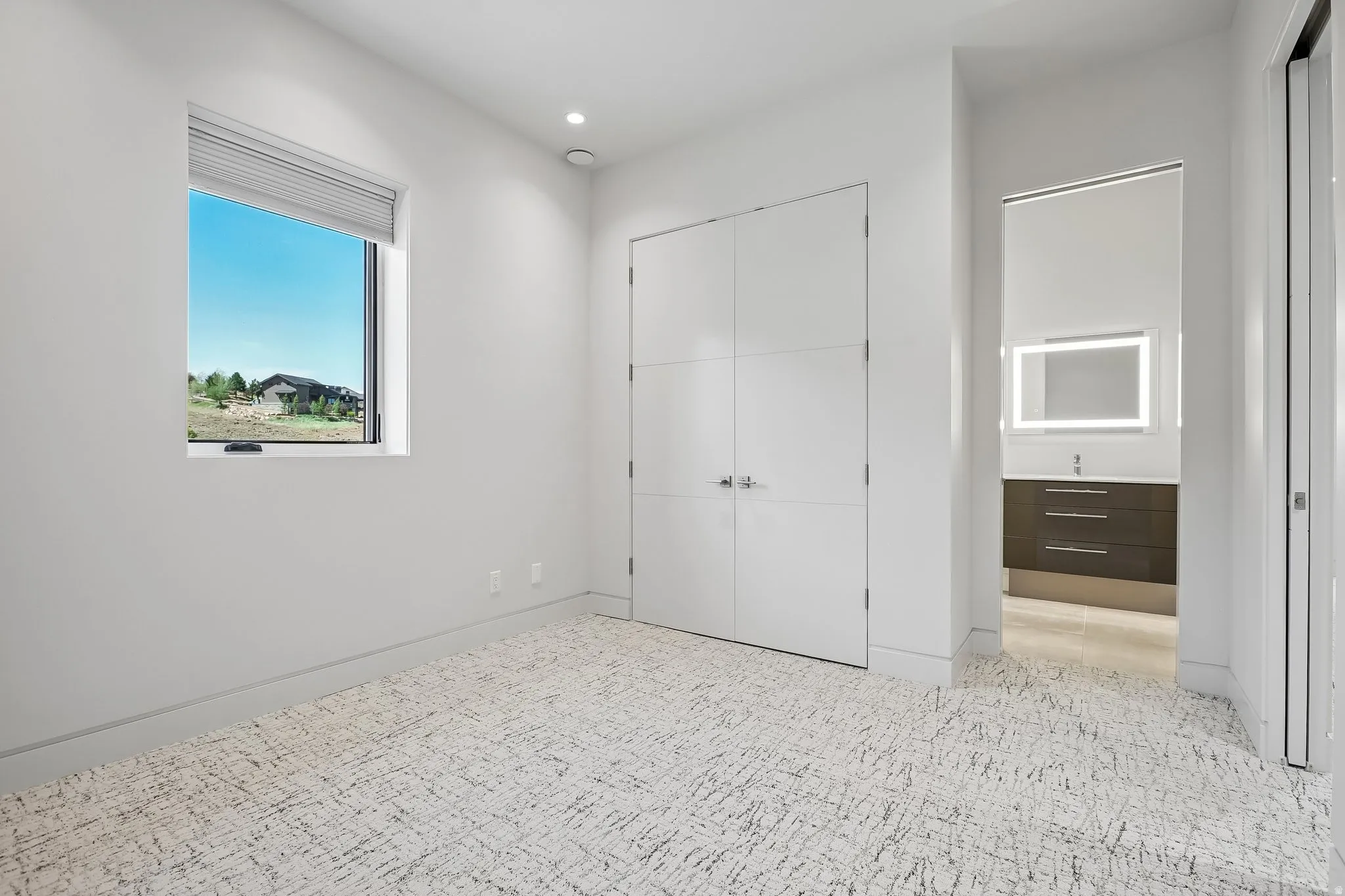 Bright interior featuring textured carpeting, a single window with blinds, recessed ceiling lighting, and a closet with double doors