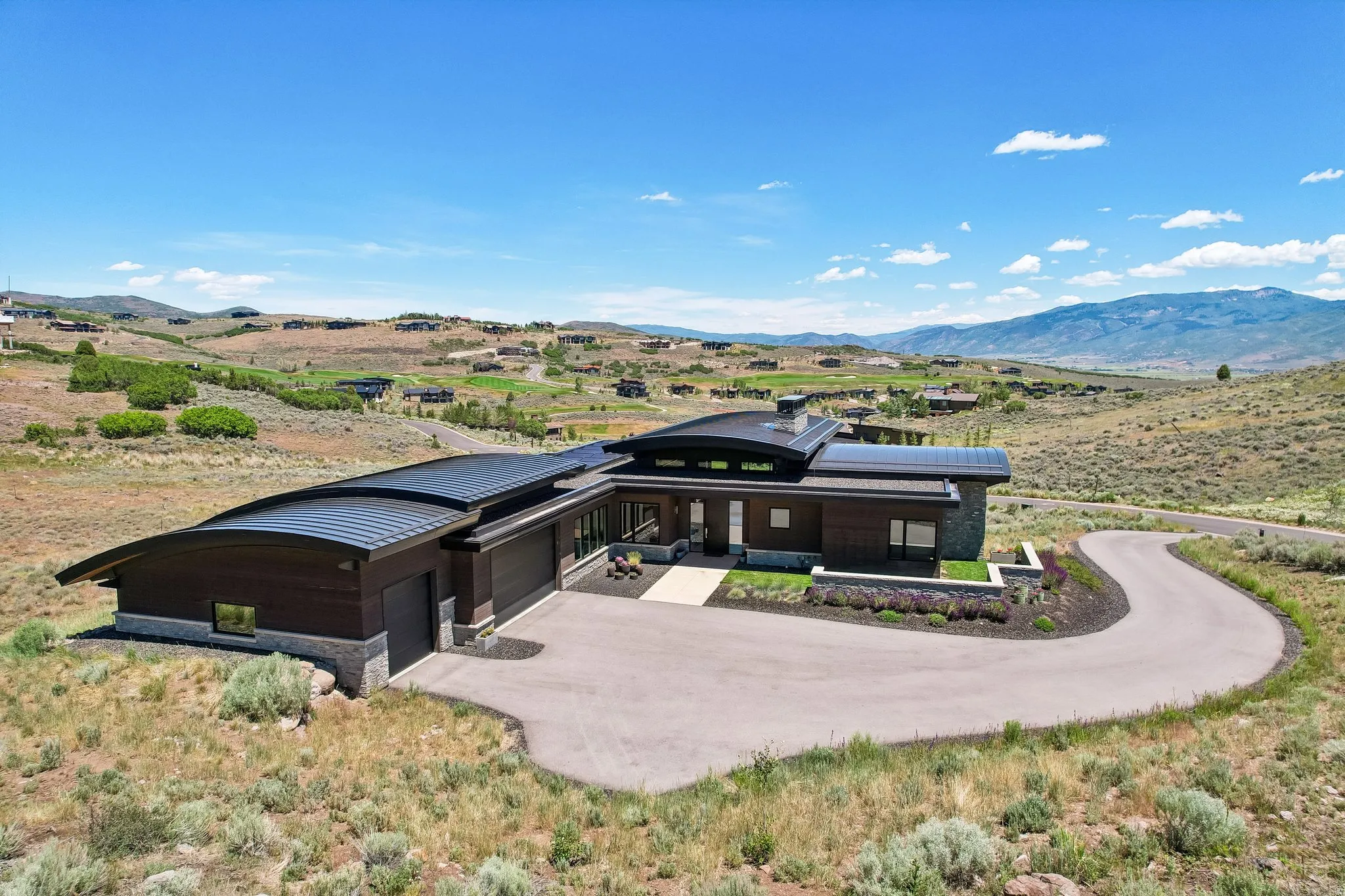 Contemporary residence featuring a curved metal roof, wood siding, and stone accents