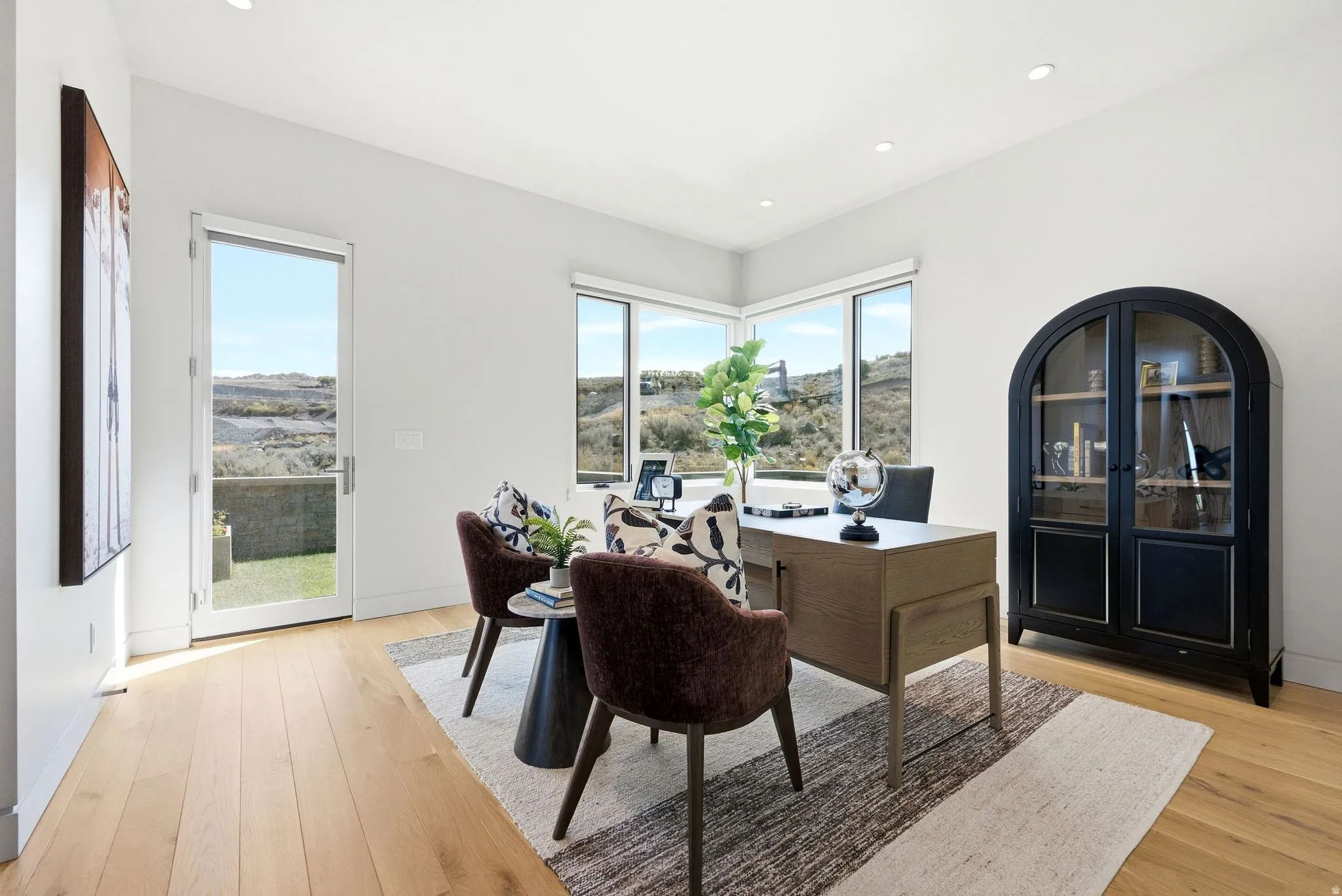 Light wood-finish flooring, recessed lighting, expansive corner windows, glass-paneled door, built-in display cabinet