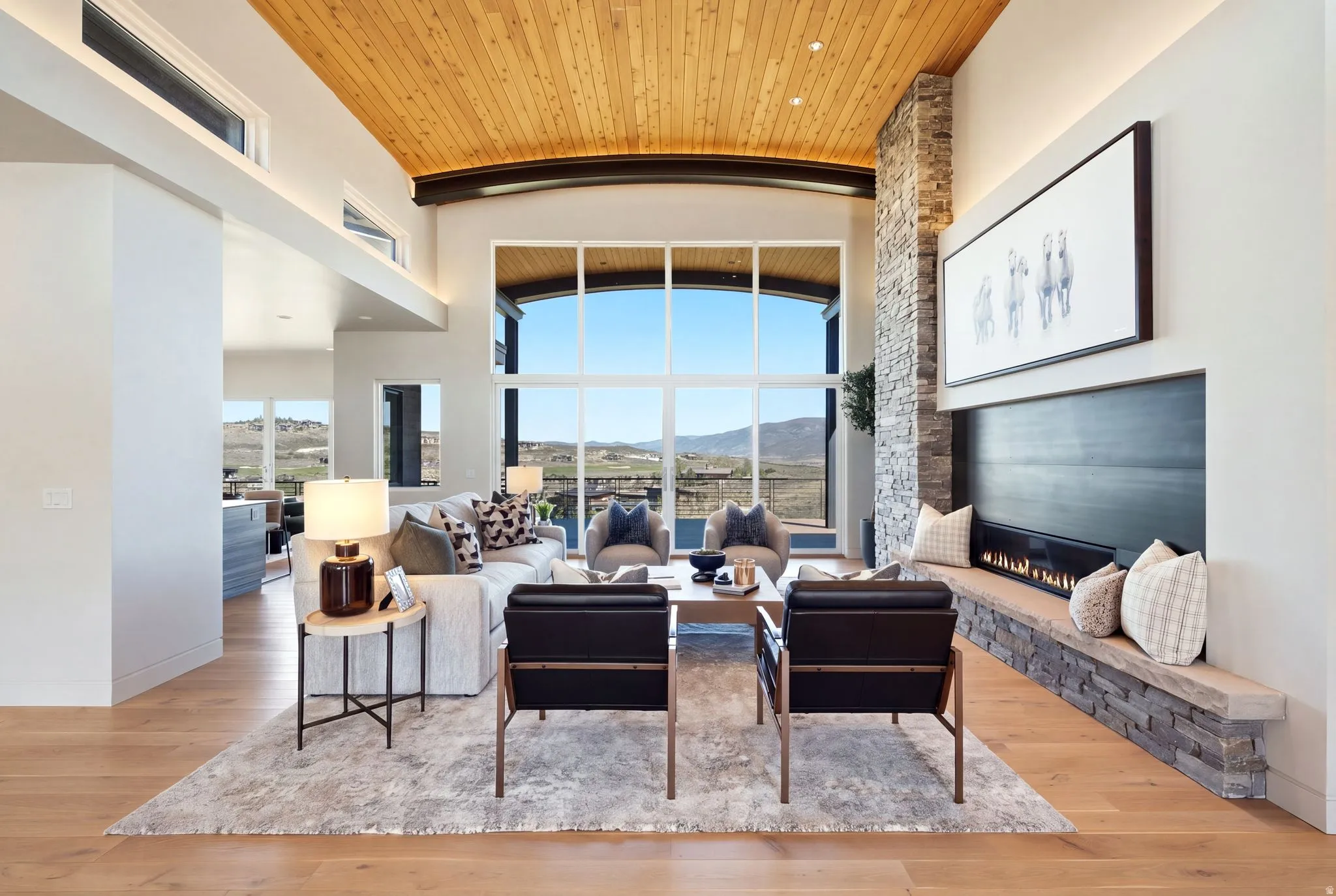 Vaulted wood-paneled ceiling, expansive two-story windows, stone-clad fireplace with hearth, recessed lighting, and wood-finish flooring