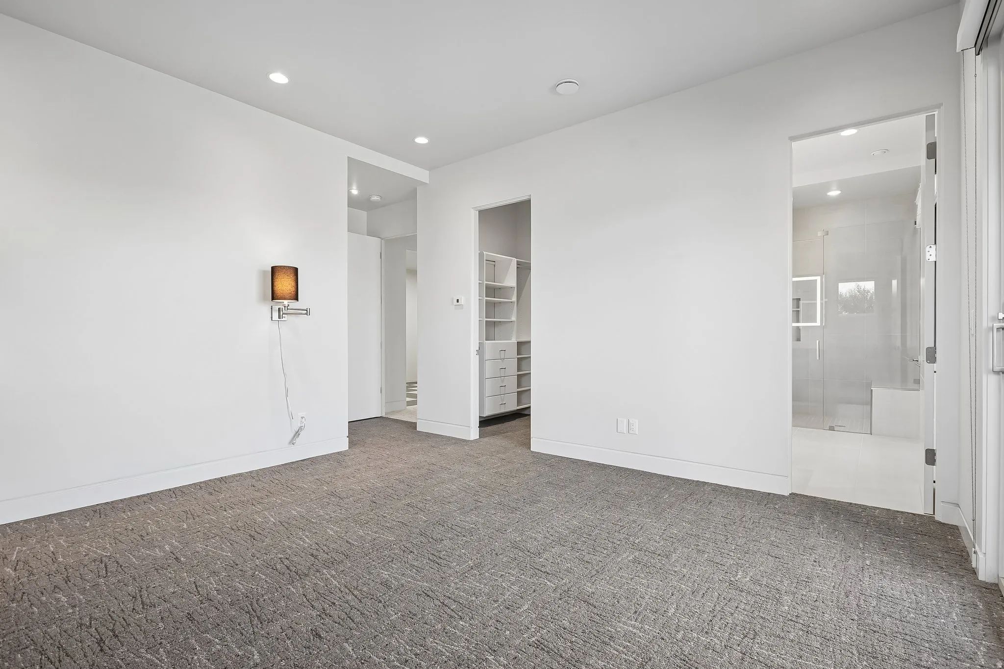Spacious room featuring textured gray carpeting, crisp white walls, recessed lighting, and a built-in closet system