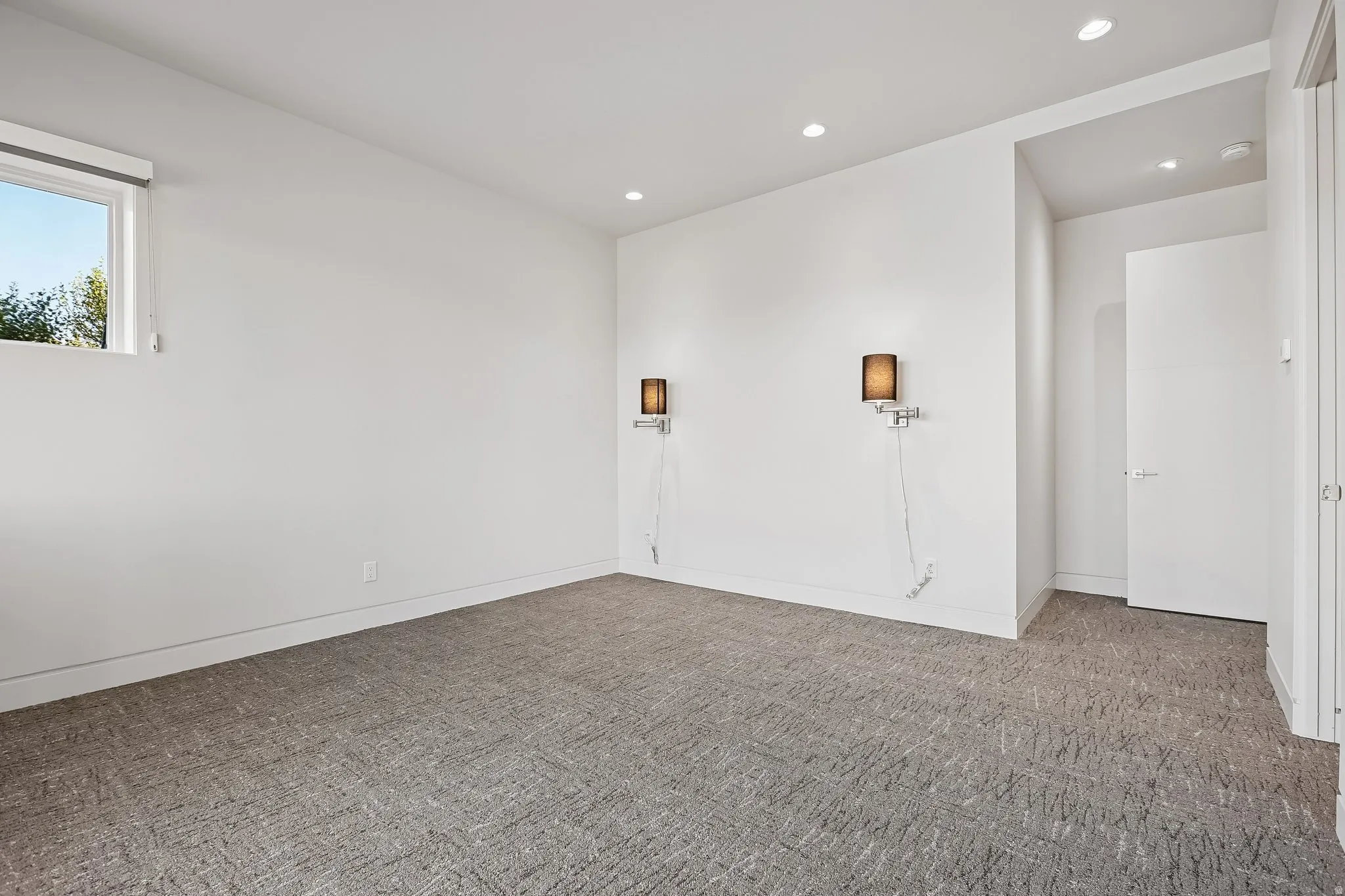 Bright room featuring recessed lighting, a modern window, two wall-mounted sconces, and neutral-toned patterned carpeting