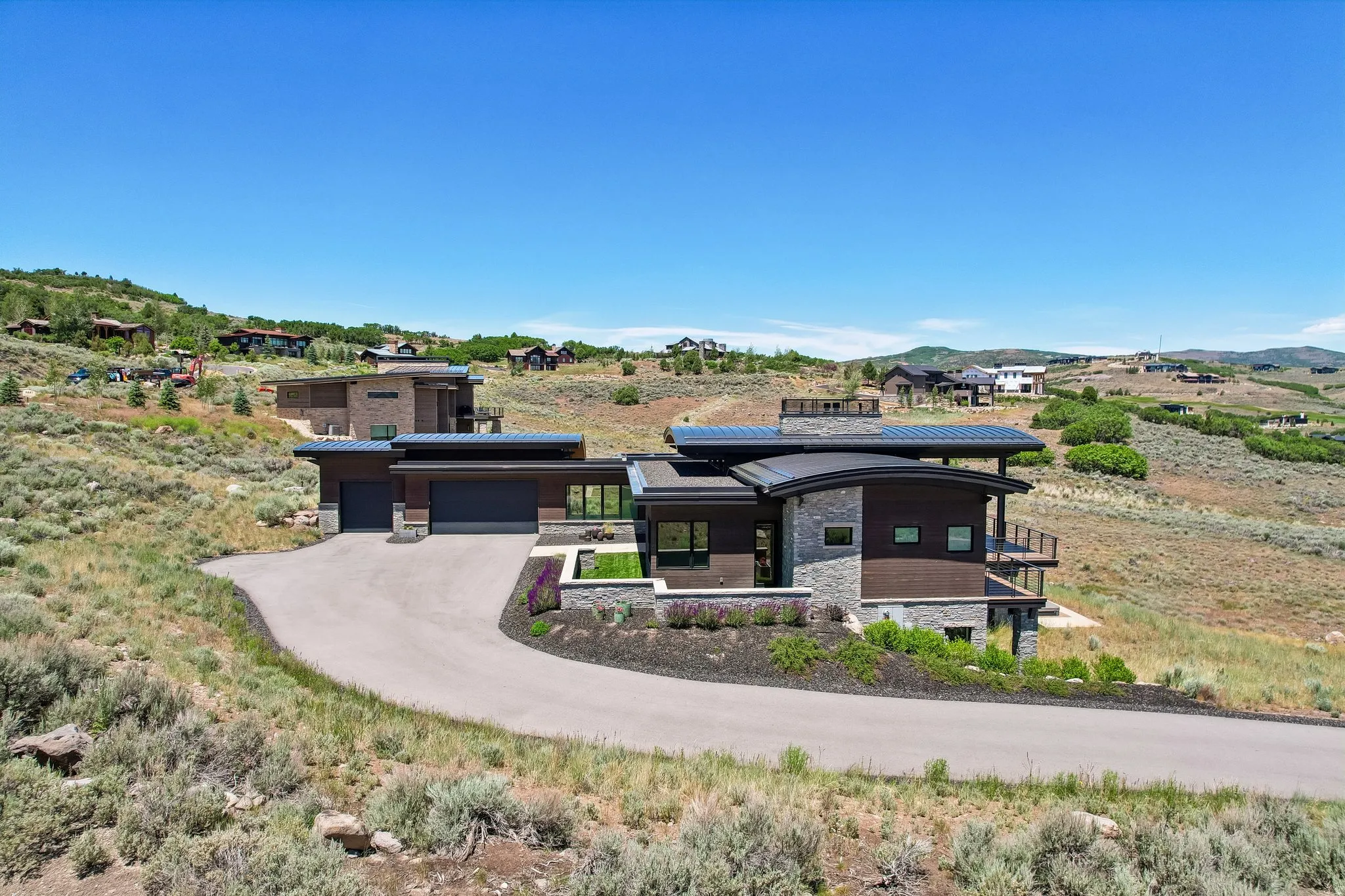 Modern architectural residence featuring stone and wood-finish siding, a curved roofline, and multiple exterior balconies